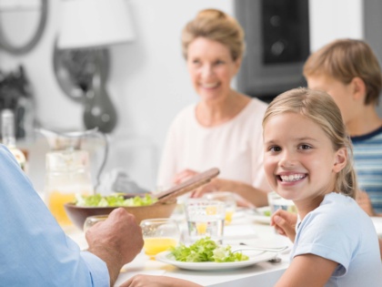 Grossmutter und Enkelkinder am Esstisch. Enkeltochter lacht und fragt, warum hast Du so viele Klammern im Mund